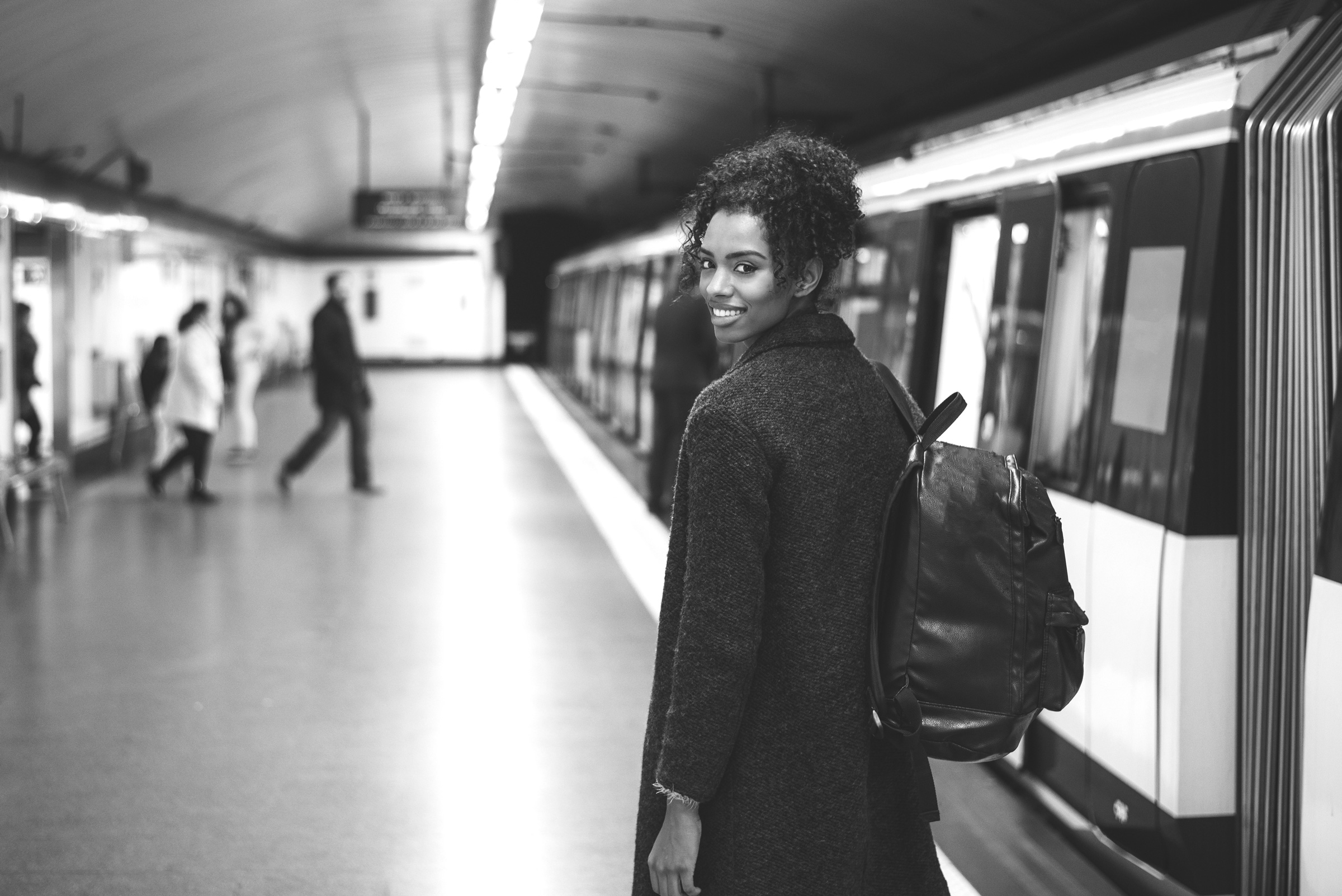 Themenbild: Junge Frau in einem unterirdischen Bahnhof am Gleis, schaut in die Kamera.