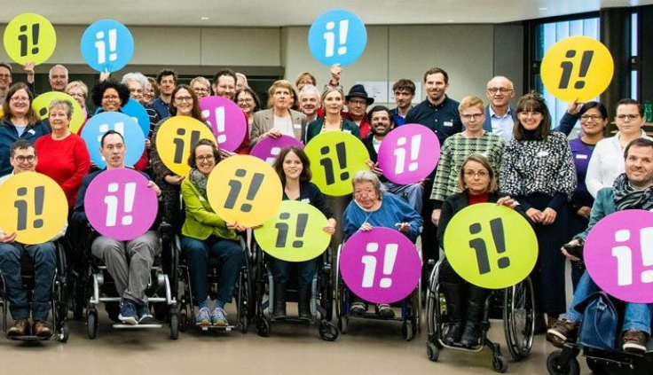 Un groupe de personnes handicapées au départ de la collecte avec des panneaux portant le logo de l'initiative d'inclusion