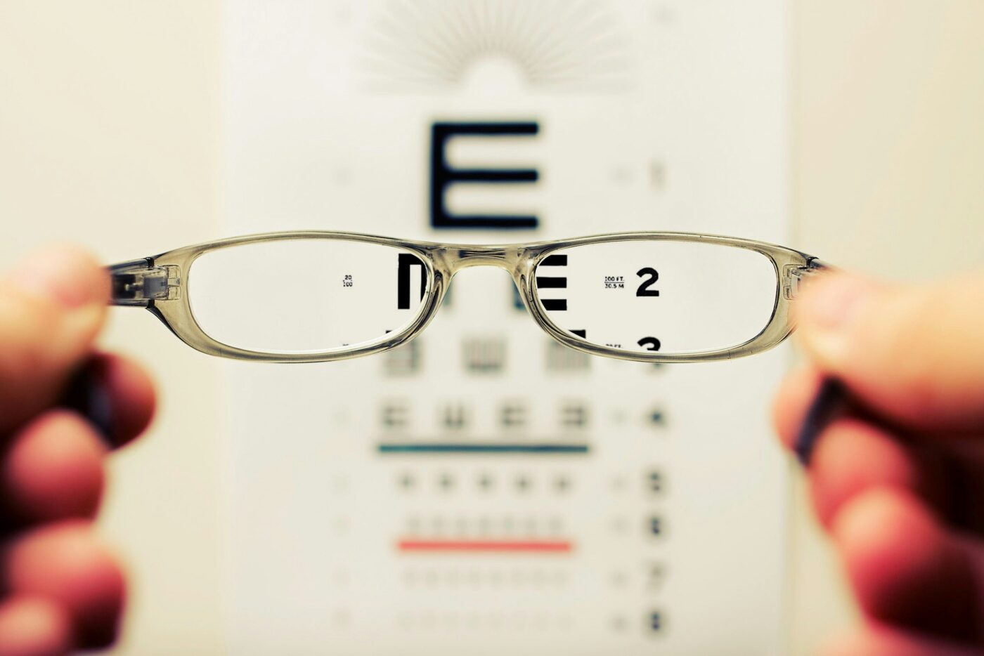 Blick durch eine Brille auf eine Sehtest-Tafel. Nur durch die Brillengläser sieht man scharf, alles andere ist verschwommen.