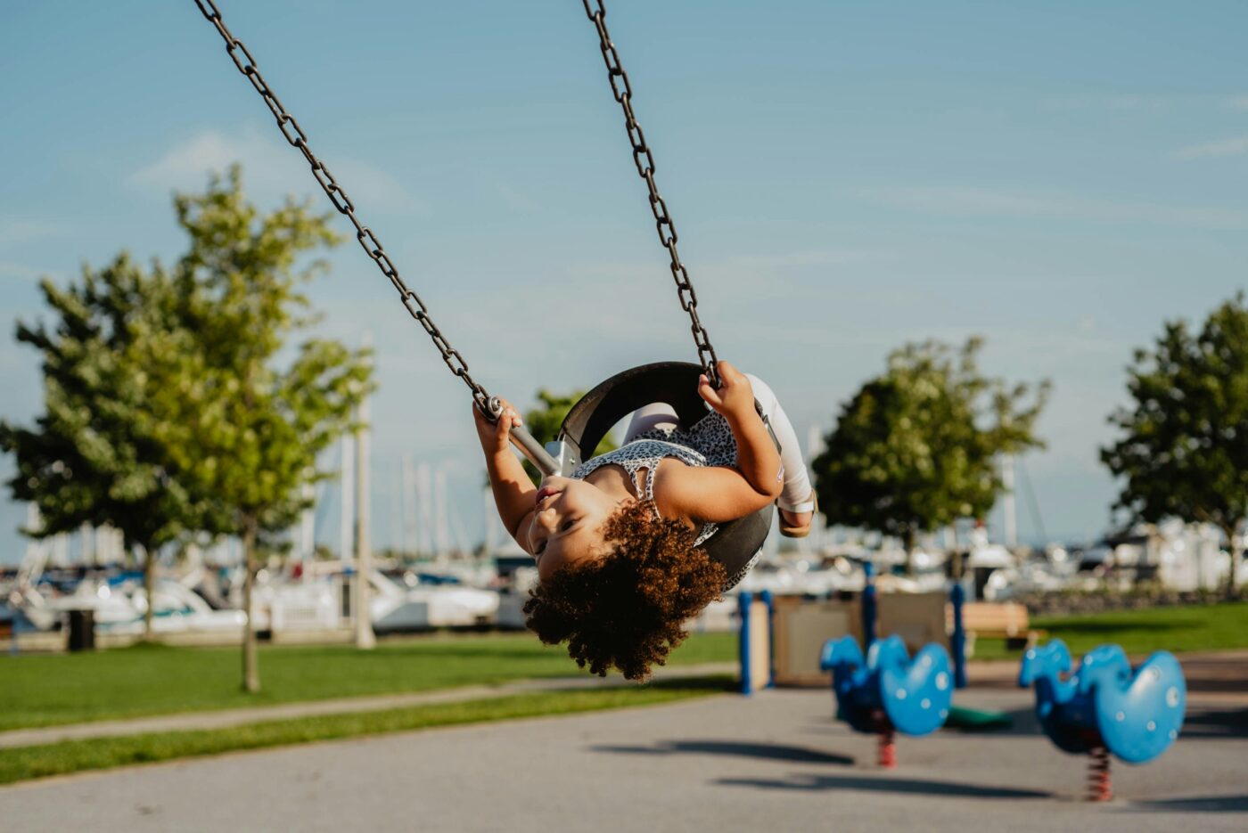 Petite fille aux cheveux bruns frisés sur la balançoire.