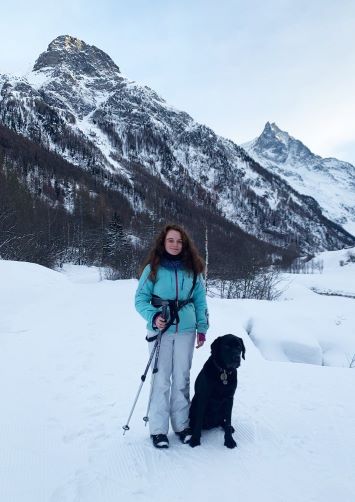 Josephine im Skianzug mit Wanderstöcken und ihrem Führhund Quinto im Schnee.