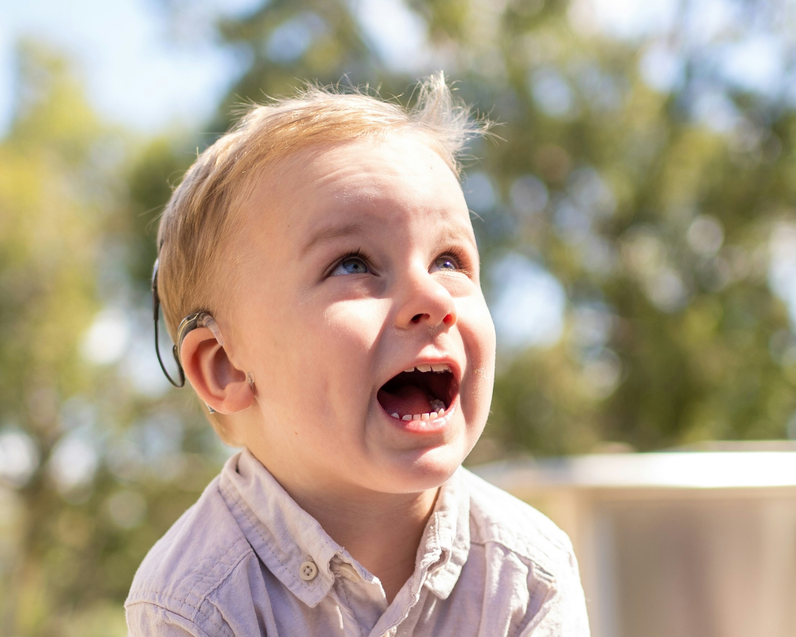 Kleiner blonder Junge mit hellem Hemd und einem Cochlea-Implantat beim Spielen.