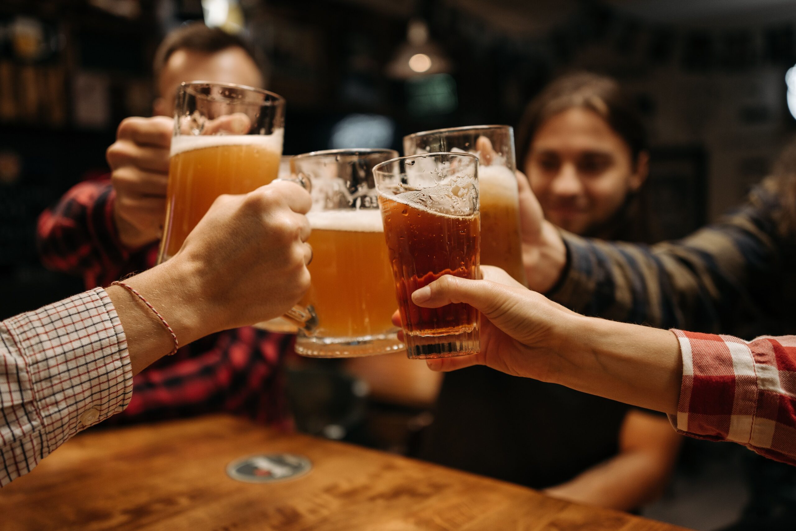 Fünf Personen sitzen um einen Tisch und stossen mit ihren Biergläsern an